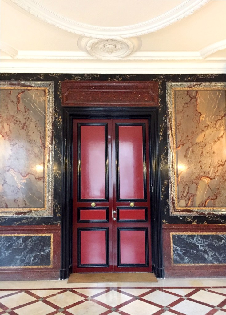 Lobby of a building in Paris, red door with colorful marble walls