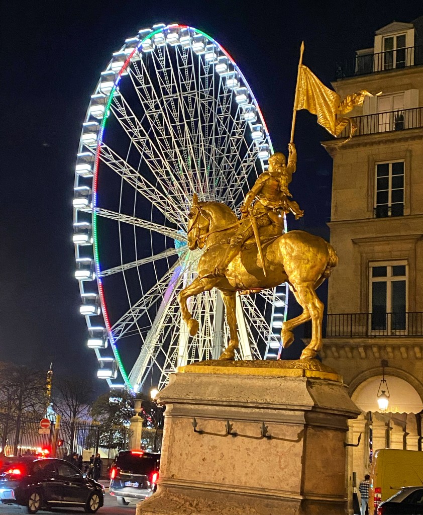 Large carousel in Paris lit up with golden statue of Joan of Arc in the foreground